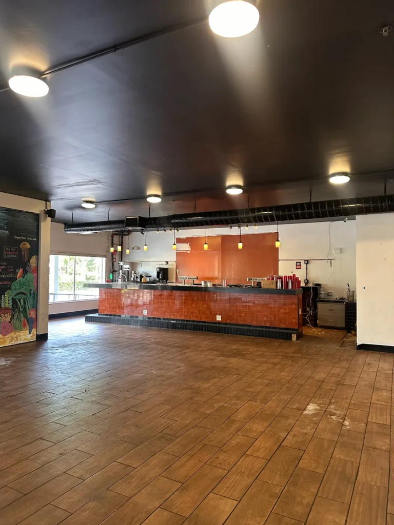 Large commercial bar space with an orange tile bar, dark ceiling, and wood-look tile floor
