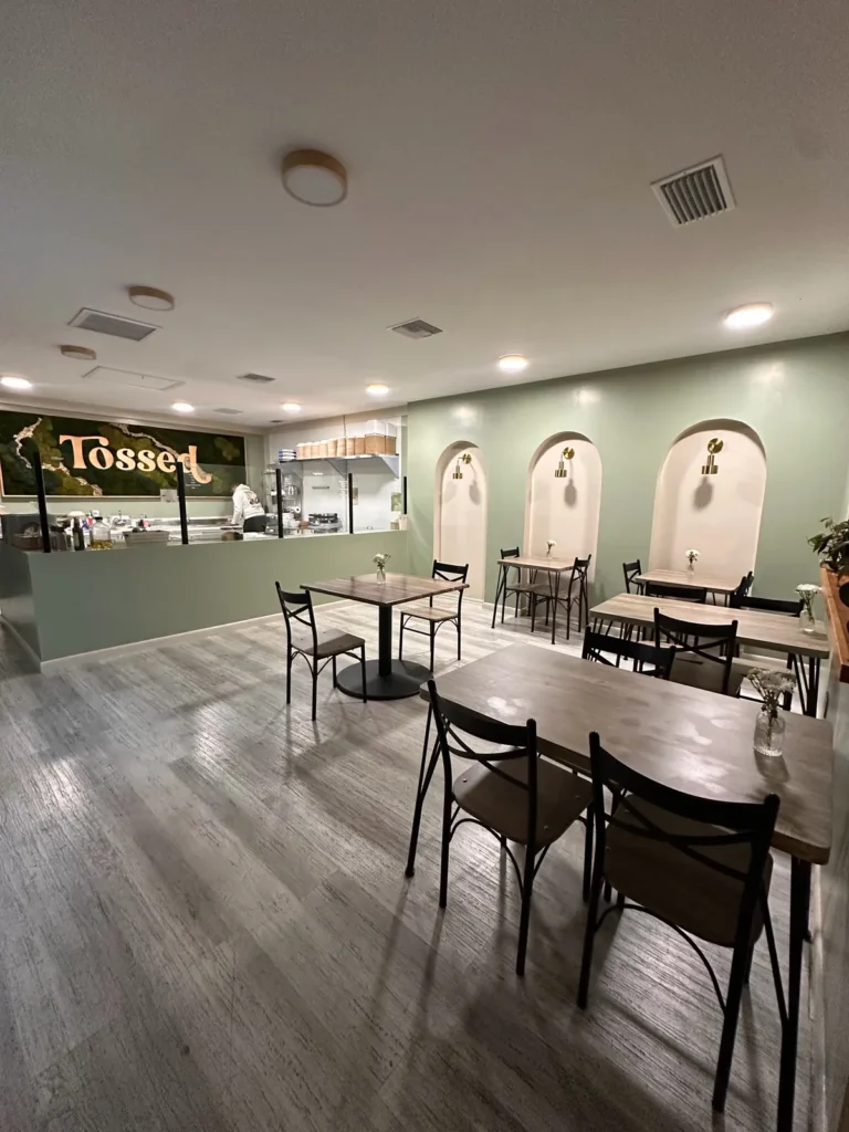 Finished restaurant dining room with sage green walls, arched wall niches, wood tables, and a service counter