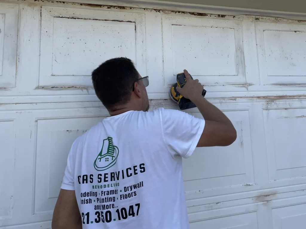 CAAS Services crew member sanding a garage door to prepare it for paint