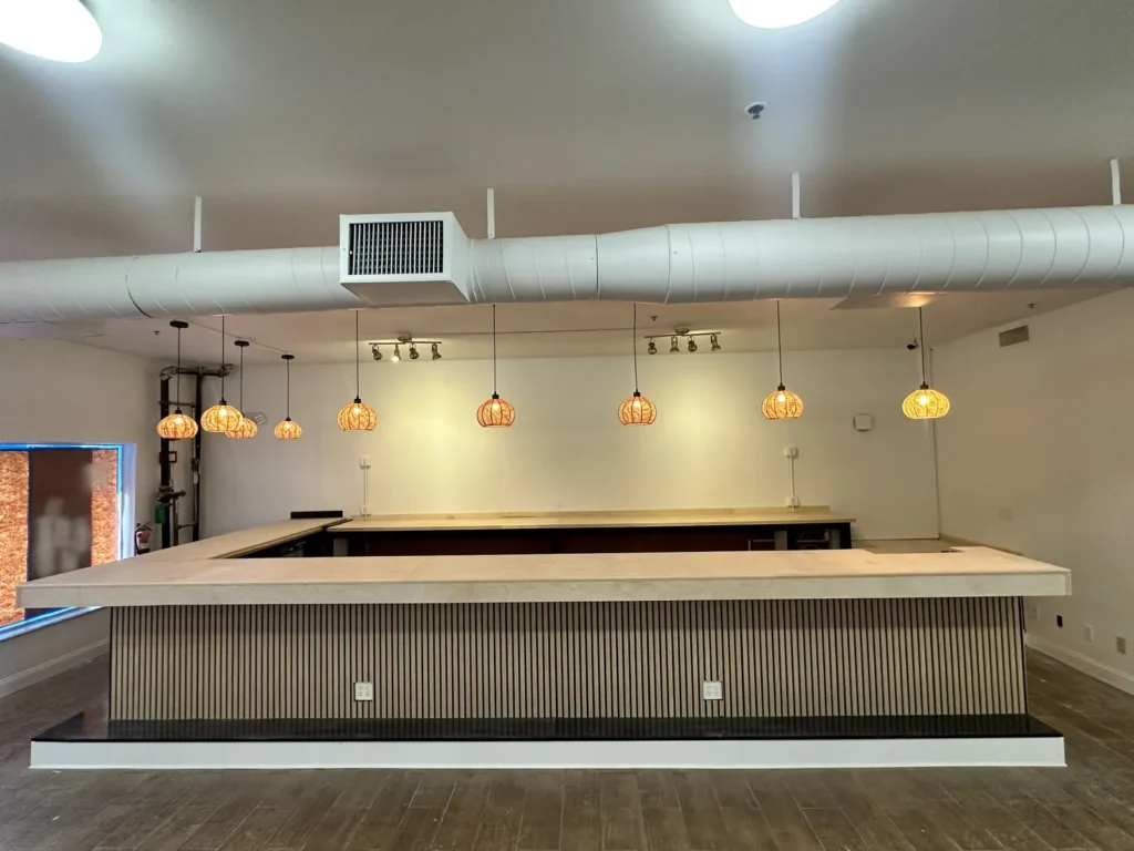 Finished commercial bar counter with light wood top, vertical wood slats, and woven pendant lights