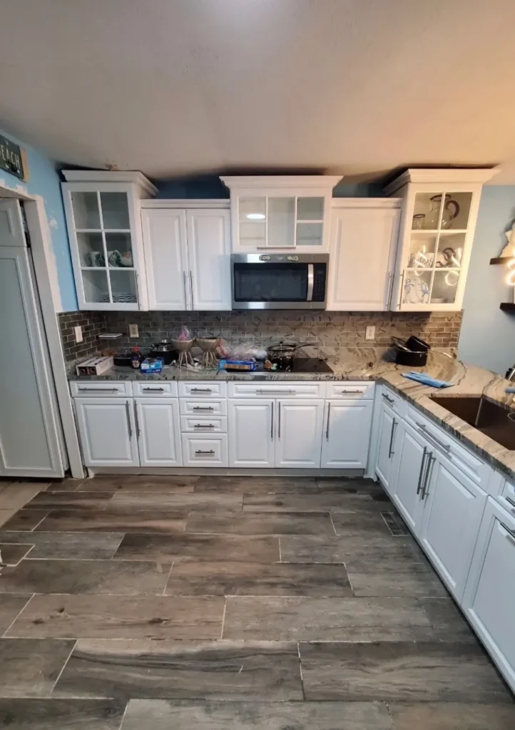 Finished kitchen with white cabinets, stone counters, and mosaic backsplash after remodel