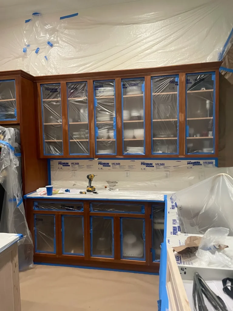 Kitchen cabinets and counters masked with plastic and blue tape before painting